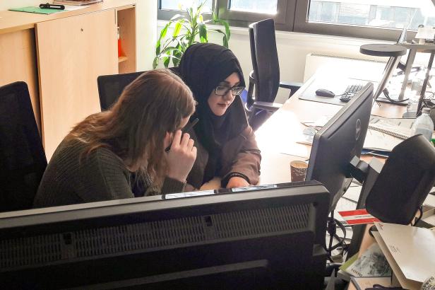 Zwei Frauen arbeiten gemeinsam an einem Schreibtisch vor einem Computer.