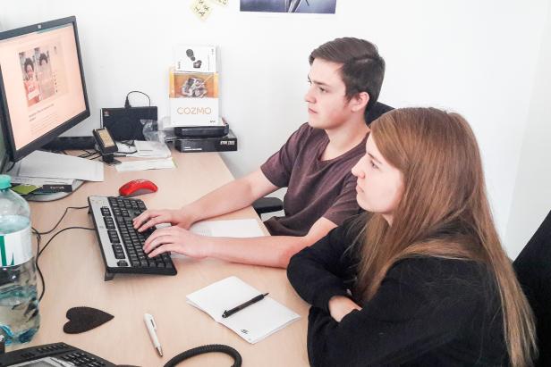 Zwei junge Leute sitzen an einem Schreibtisch und arbeiten am Computer.