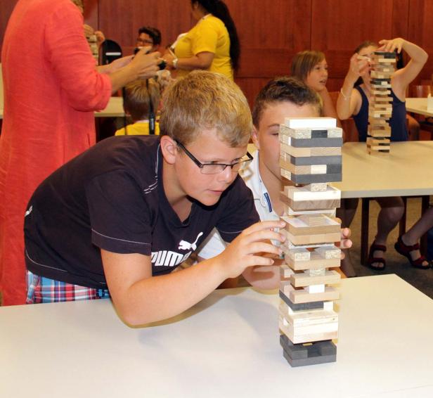 Ein Junge mit Brille spielt mit einem Holzklotz-Turm, während andere Kinder zusehen.