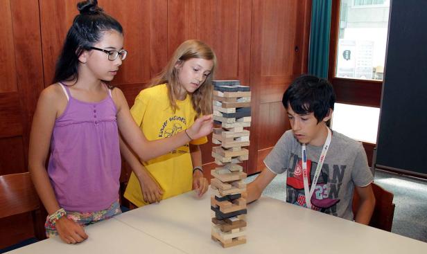Drei Kinder spielen mit einem Jenga-Turm an einem Tisch.