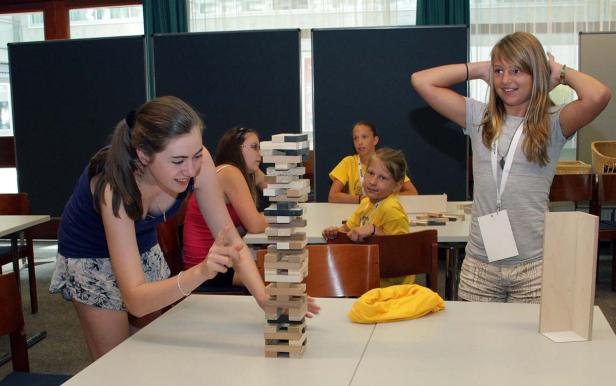 Eine Gruppe von Mädchen spielt mit einem Holzklotz-Turm an einem Tisch.