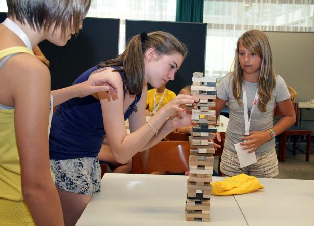 Drei junge Frauen spielen ein Geschicklichkeitsspiel mit Holzklötzen.