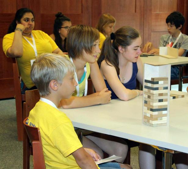 Eine Gruppe Jugendlicher sitzt an einem Tisch und spielt ein Geschicklichkeitsspiel.