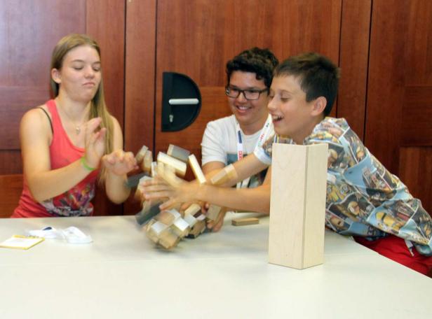 Drei Jugendliche spielen mit Holzklötzen an einem Tisch.