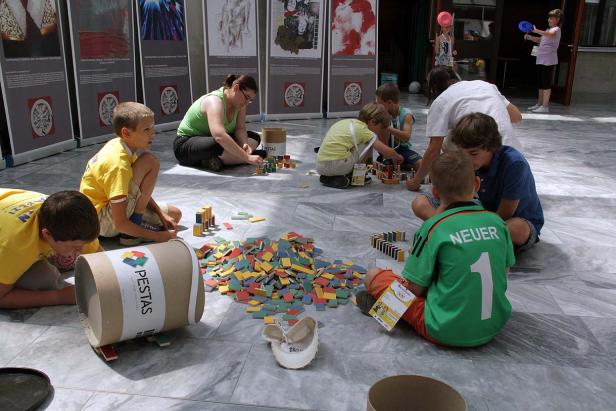 Kinder und eine Frau spielen mit bunten Holzbausteinen auf dem Boden.