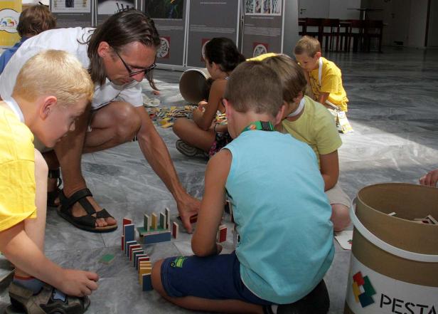 Eine Gruppe Kinder und ein Erwachsener spielen mit Dominosteinen auf dem Boden.
