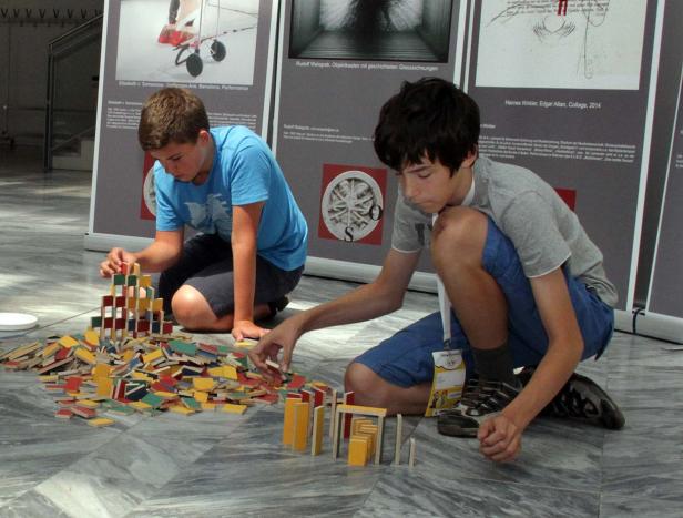 Zwei Jungen bauen Türme aus bunten Holzplättchen vor Kunstwerken.