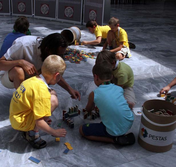 Eine Gruppe Kinder spielt mit einem Erwachsenen auf dem Boden mit bunten Holzbausteinen.