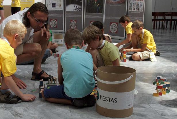 Eine Gruppe Kinder und ein Erwachsener spielen mit bunten Holzbausteinen auf dem Boden.