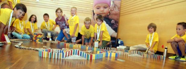 Eine Gruppe Kinder baut gemeinsam eine lange Domino-Kette auf einem Holzboden.