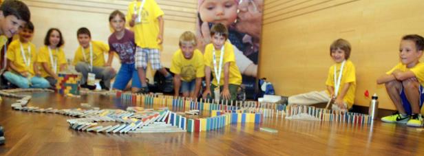 Eine Gruppe Kinder baut eine lange Domino-Kette auf einem Holzboden.