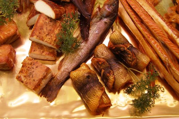 Verschiedene geräucherte Fischprodukte auf einer goldenen Platte angerichtet.