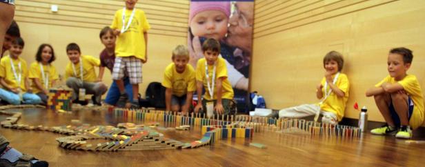 Eine Gruppe Kinder baut eine lange Domino-Kette auf einem Holzboden.