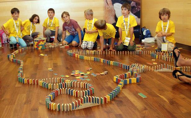 Eine Gruppe Kinder baut eine lange Domino-Kette auf einem Holzboden.