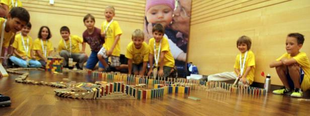 Eine Gruppe Kinder baut eine lange Domino-Kette auf einem Holzboden.