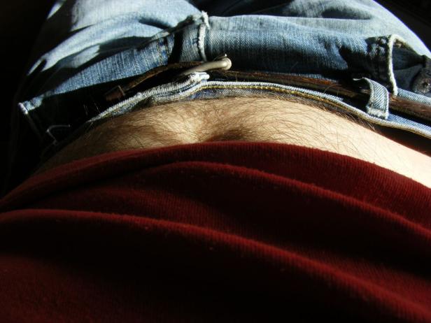 Ein Mann liegt mit Jeans und rotem T-Shirt da, die Bauchpartie ist sichtbar.