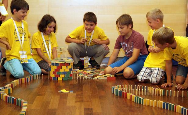 Eine Gruppe Kinder spielt mit Dominosteinen auf einem Holzboden.