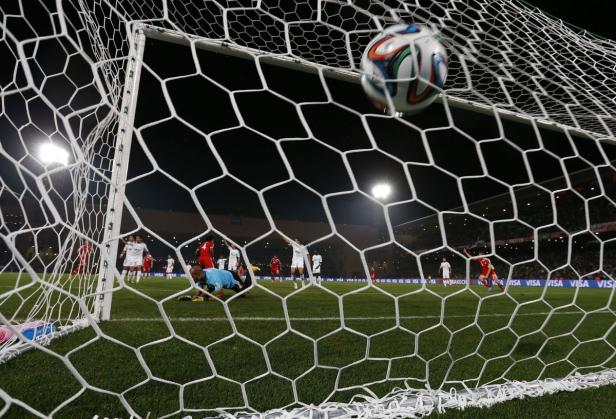 Ein Fußball fliegt ins Netz, während der Torwart am Boden liegt.
