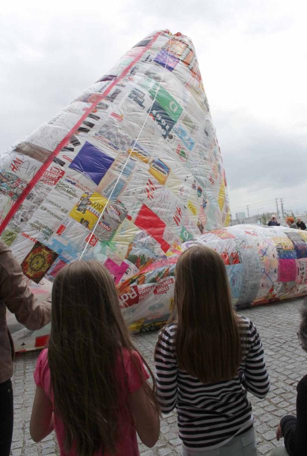 Zwei Mädchen stehen vor einer großen, pyramidenförmigen Skulptur aus recycelten Materialien.