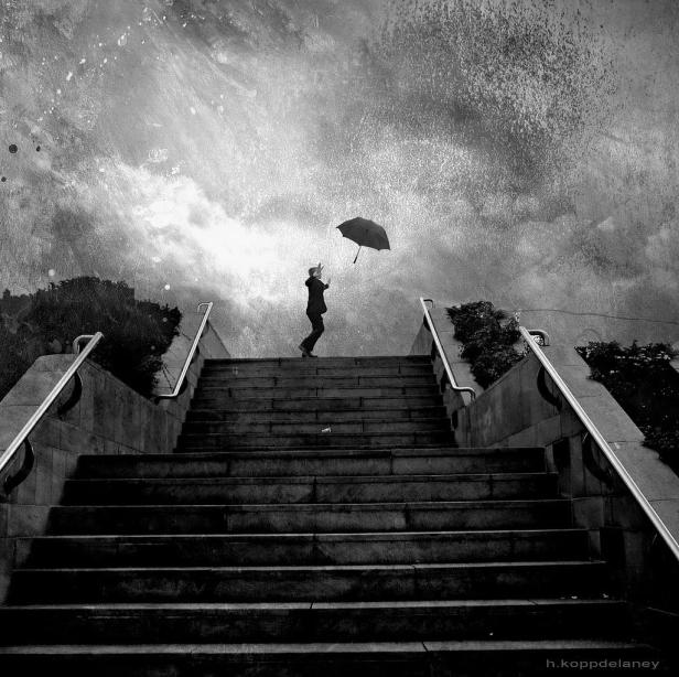 Eine Person mit Regenschirm steht auf einer Treppe unter einem bewölkten Himmel.