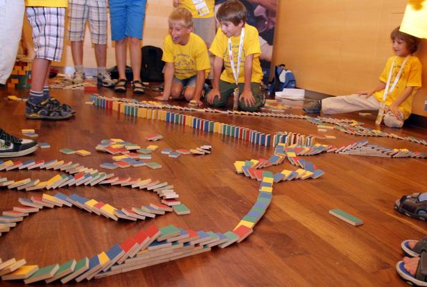 Kinder bauen eine lange Domino-Kette auf einem Holzboden.