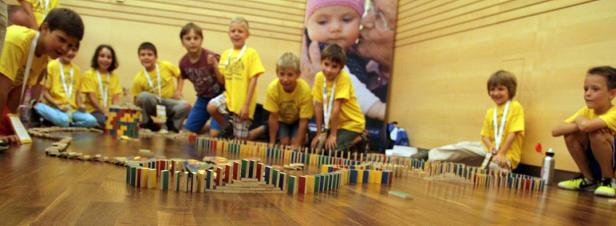 Eine Gruppe Kinder baut gemeinsam eine Domino-Kette auf einem Holzboden.