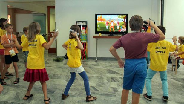 Eine Gruppe Kinder tanzt vor einem Bildschirm, auf dem „Just Dance“ läuft.