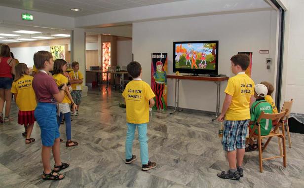 Eine Gruppe Kinder schaut auf einen Fernseher, auf dem „Just Dance“ läuft.