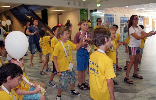 Eine Gruppe Kinder in gelben T-Shirts versammelt sich in einem hellen Raum.