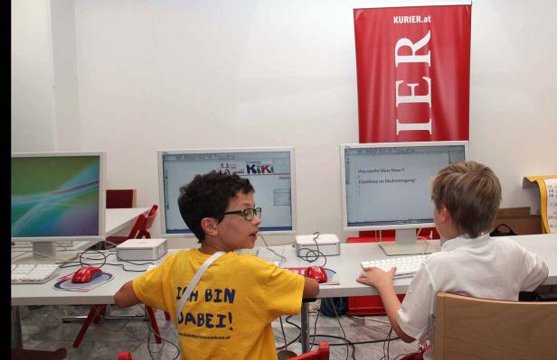 Zwei Kinder sitzen an Computern; im Hintergrund ein „Kurier.at“-Banner.