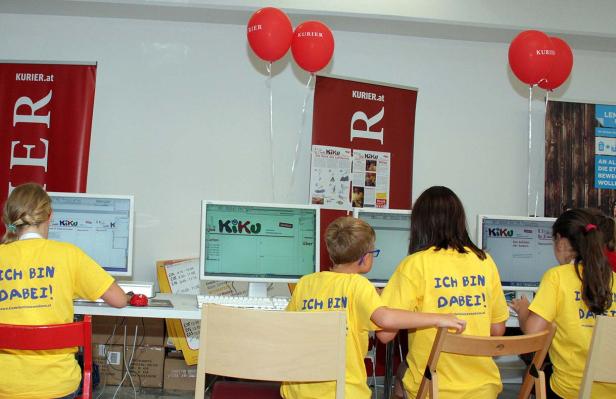 Kinder sitzen vor Computern mit dem Logo von KiKu und tragen gelbe T-Shirts mit der Aufschrift „Ich bin dabei!“.