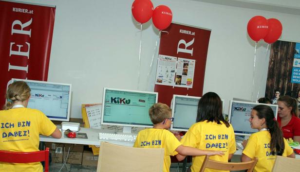 Kinder sitzen an Computern mit „Ich bin dabei!“-T-Shirts bei einer Veranstaltung von Kurier.at.