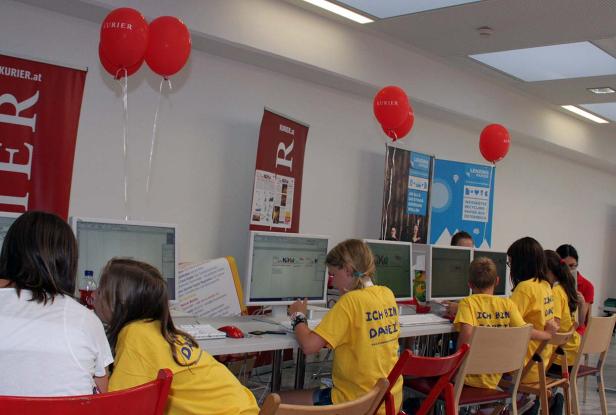 Kinder sitzen an Computern bei einer Veranstaltung des „Kurier“ und „Lenzing Papier“.