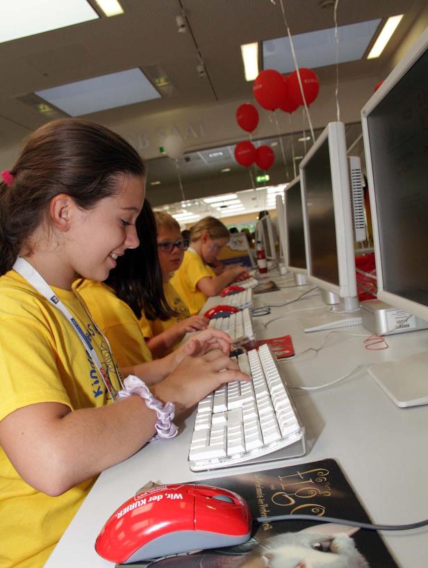 Kinder sitzen an Computern und tippen auf Tastaturen.