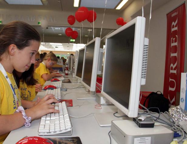 Ein Mädchen tippt an einem Computer bei einer Veranstaltung mit roten Luftballons und einem „Kurier“-Banner.