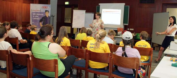 Kinder sitzen in einem Raum und hören einem Vortrag zu.
