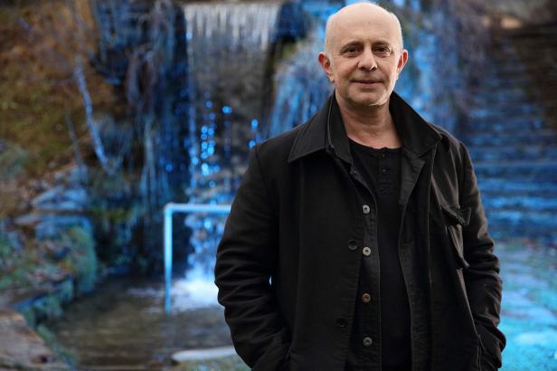 Ein Mann mit dunkler Jacke steht vor einem Wasserfall.