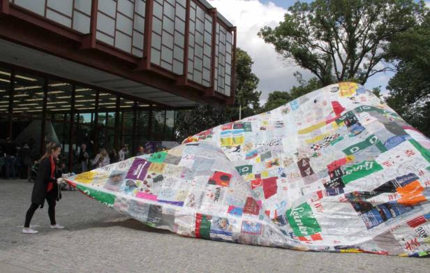 Eine Frau zieht an einer großen, mit Logos beklebten Plane vor einem Gebäude.
