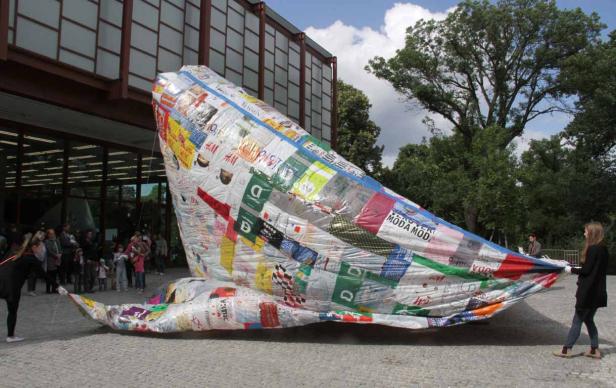 Eine große, walartige Skulptur aus recycelten Einkaufstüten vor einem Gebäude.