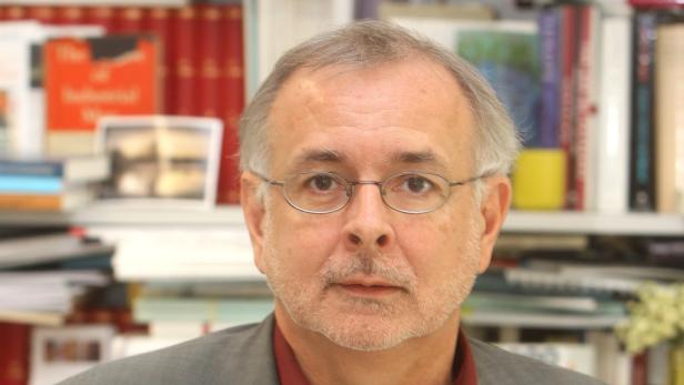 Porträt eines Mannes mit Brille vor einem Bücherregal.