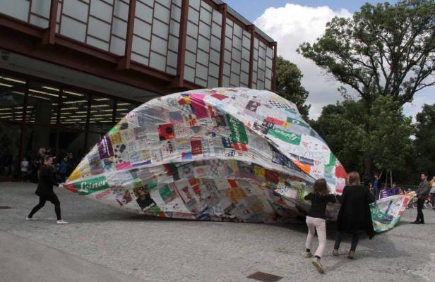 Mehrere Personen tragen eine große, mit Collagen bedeckte Plane vor einem Gebäude.