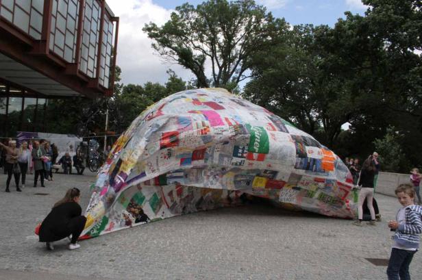 Eine Kuppel aus recycelten Materialien steht vor einem Gebäude, umgeben von Menschen.