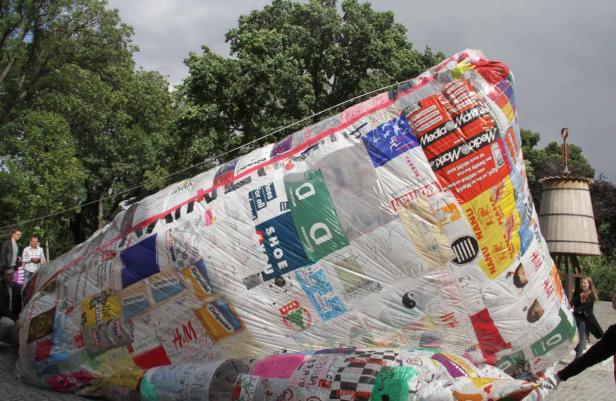 Ein großes, mit Logos und Schriftzügen beklebtes Objekt liegt im Freien.