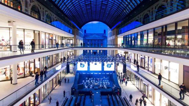 Blick in ein mehrstöckiges Einkaufszentrum mit Bühne und Publikum.