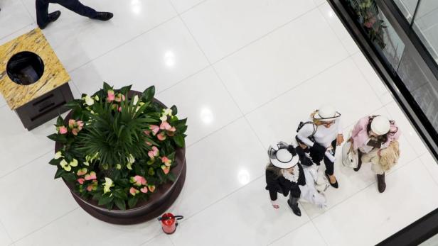 Drei Frauen mit Hüten stehen in einem Einkaufszentrum in der Nähe eines Blumenkübels.