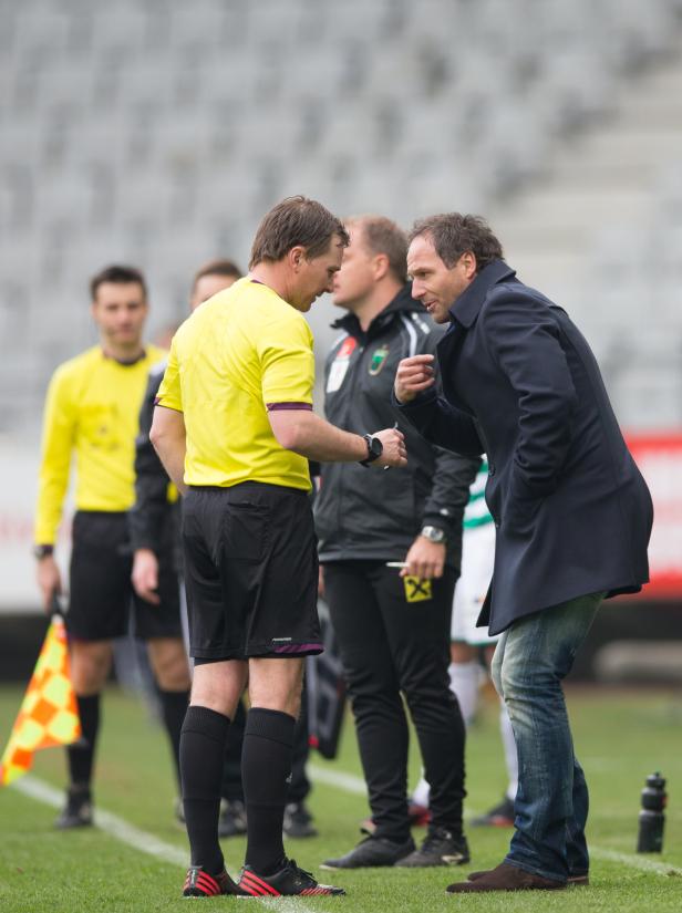 Ein Schiedsrichter diskutiert auf dem Spielfeld mit einem Trainer.