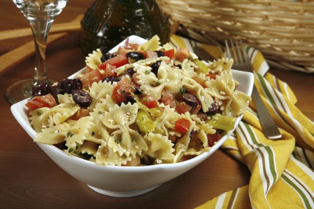 Ein Schüssel mit Farfalle-Nudelsalat mit Tomaten, Oliven und Peperoni.
