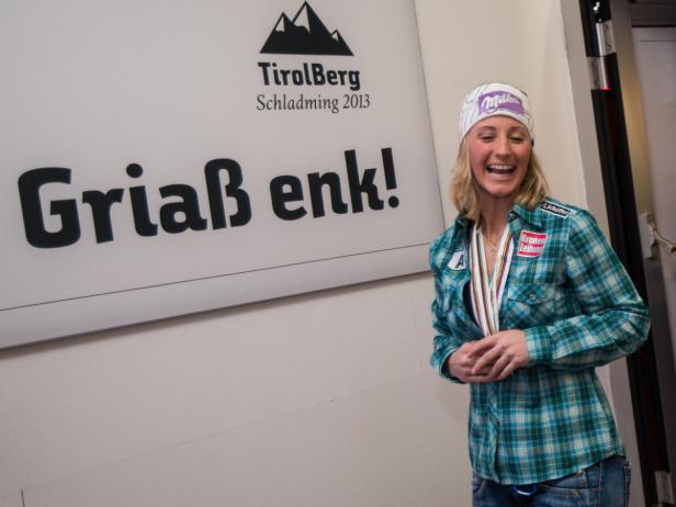 Eine lächelnde Sportlerin mit Medaillen vor einem „TirolBerg Schladming 2013“-Schild.