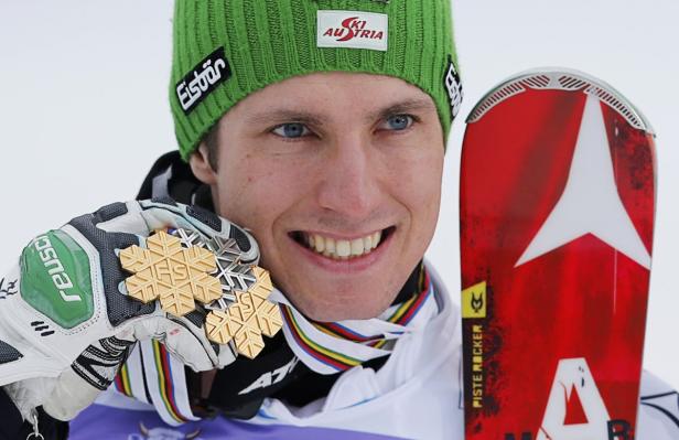 Ein lächelnder Skirennläufer mit Goldmedaillen und einem Ski.