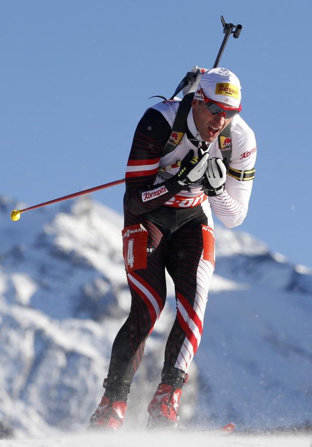 Ein Biathlet läuft auf Skiern vor einer verschneiten Bergkulisse.